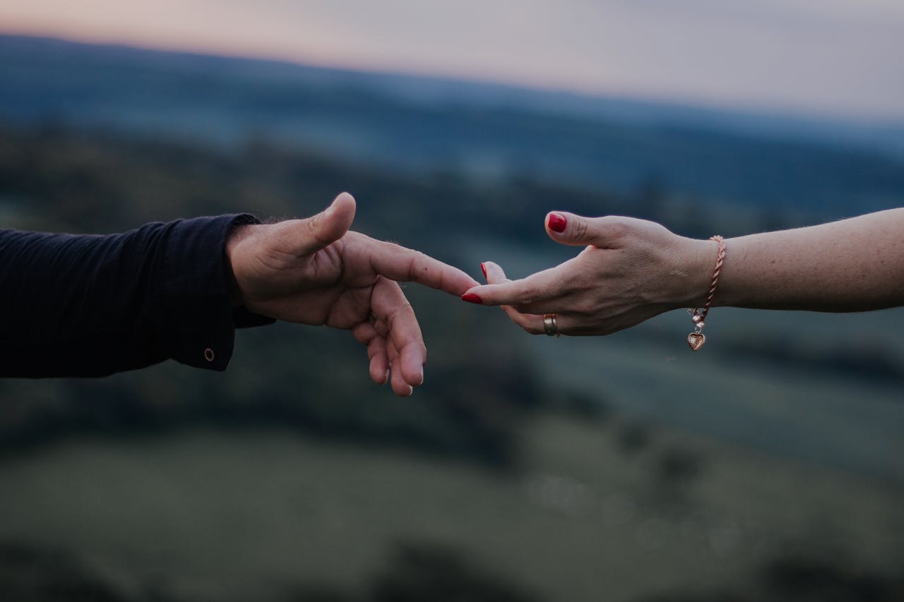 A romantic moment with hands reaching out in a peaceful outdoor setting captured at twilight.