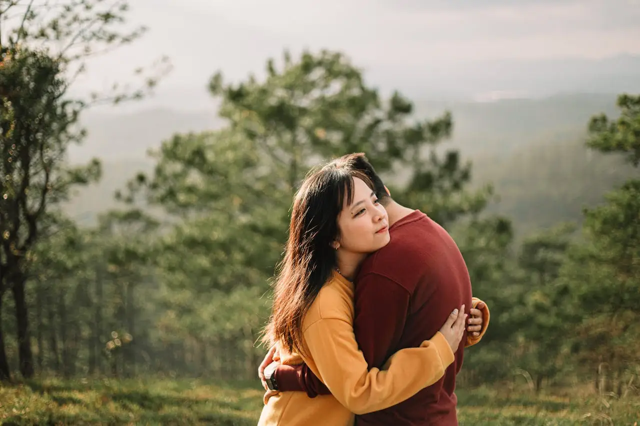 Young couple hugging peacefully in a forested area with sunlight.