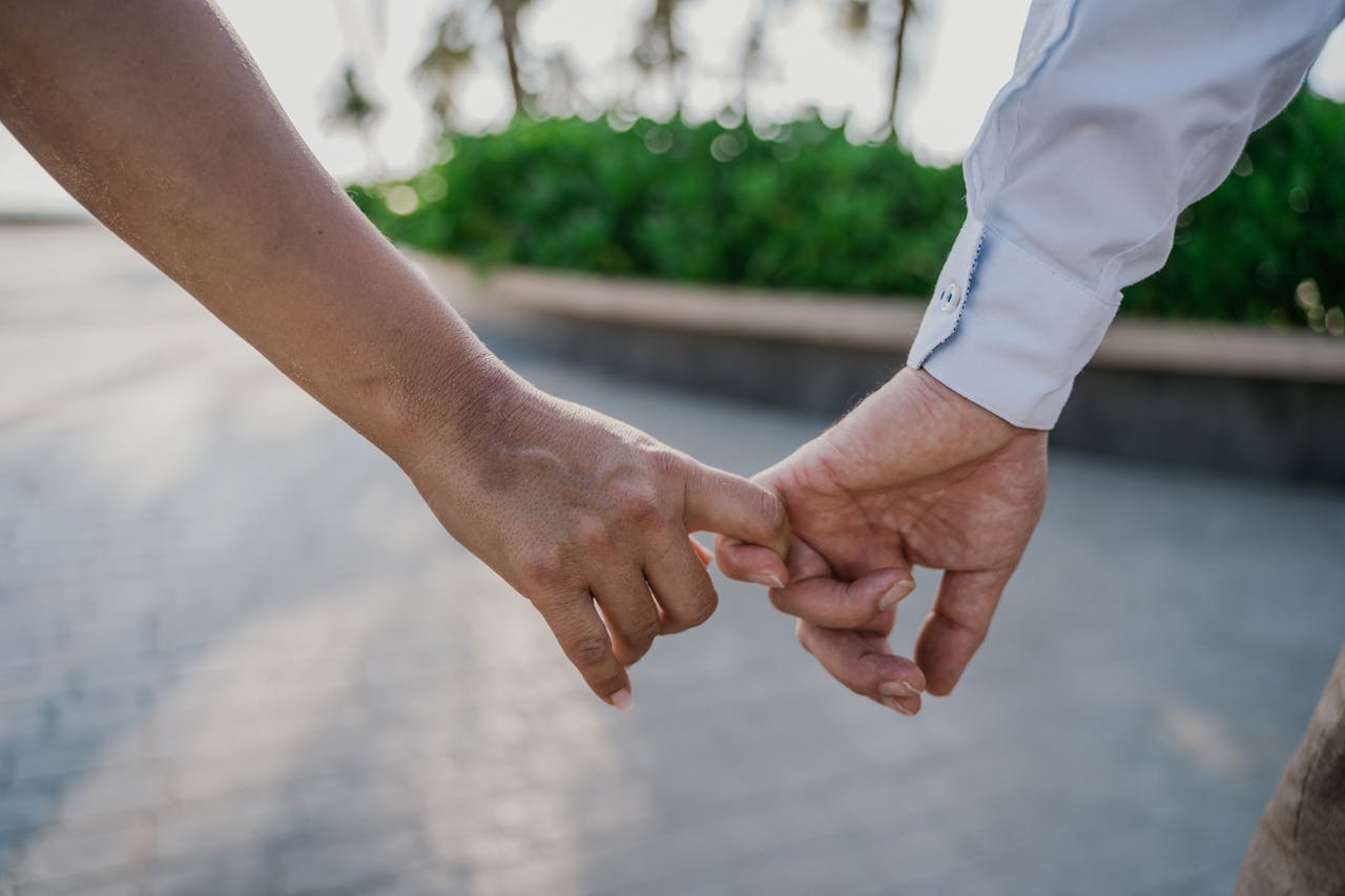 Close-up of a couple gently holding hands outdoors, symbolizing love and connection.